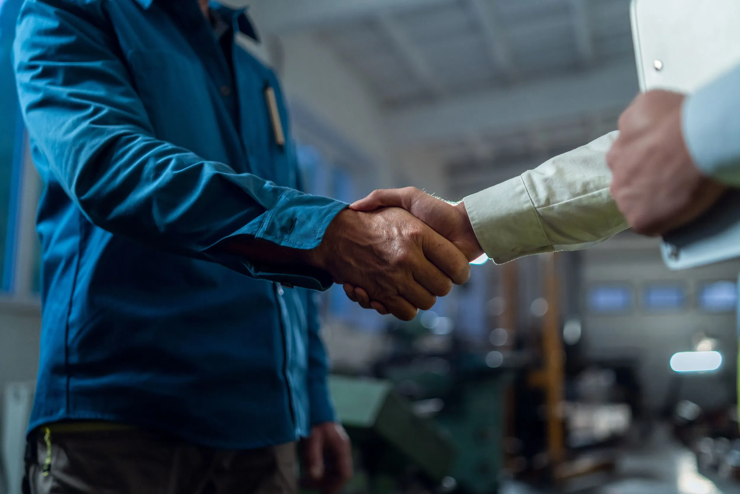 Close-up of engineer shaking hands with mature worker indoors in metal workshop.