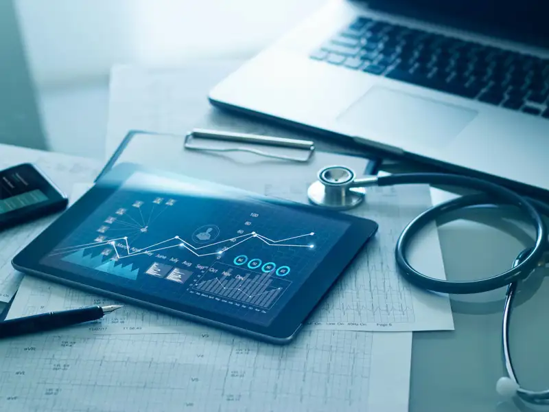 Stethoscope, laptop and a tablet on a desk.